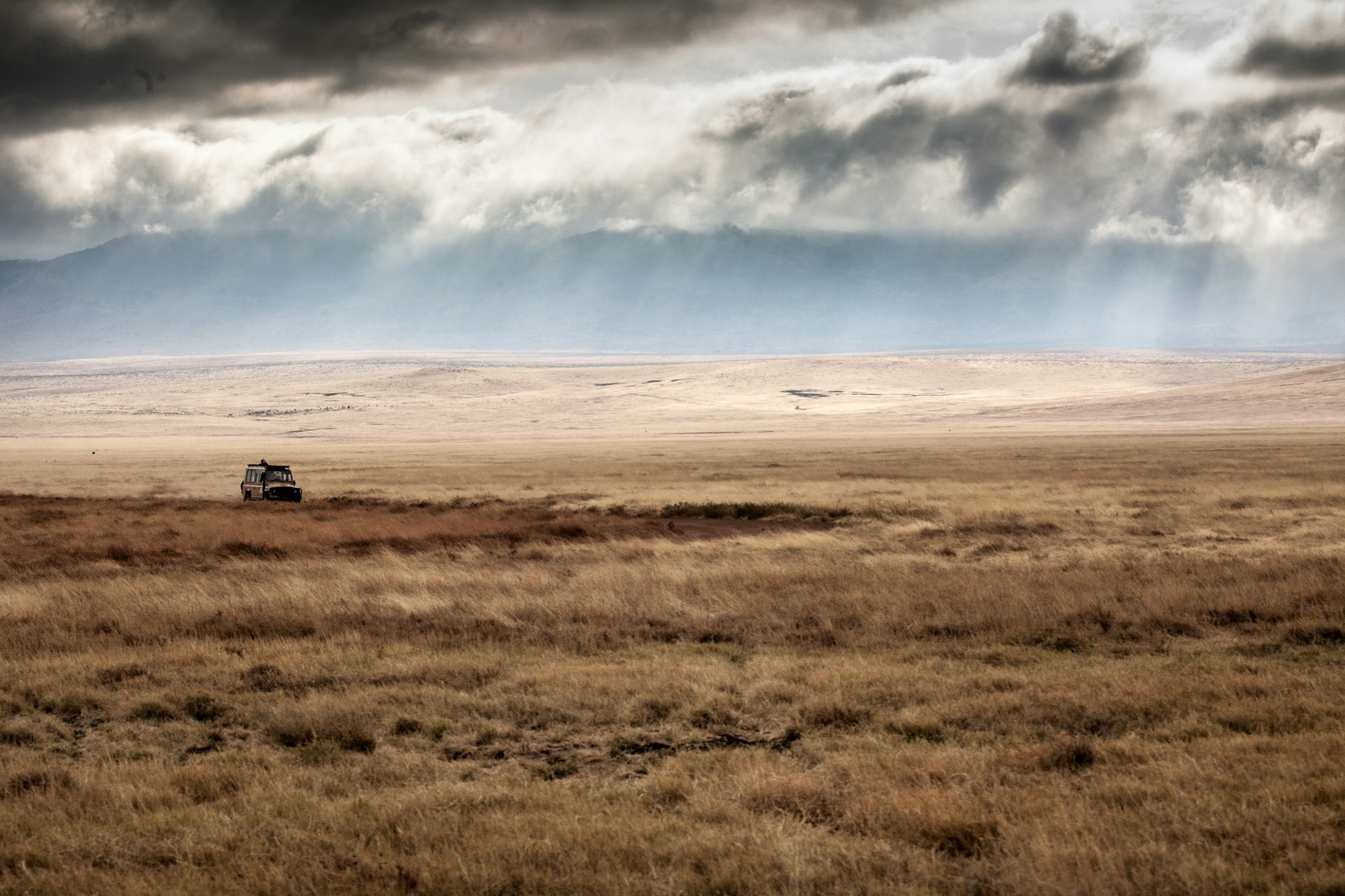 a vehicle passing through dry field under black clouds